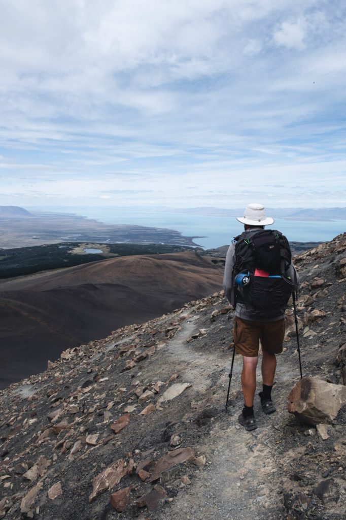 Ein Mann mit Rucksack wandert auf einem schmalen Bergpfad in El Chaltén mit Aussiicht auf den Viedema See